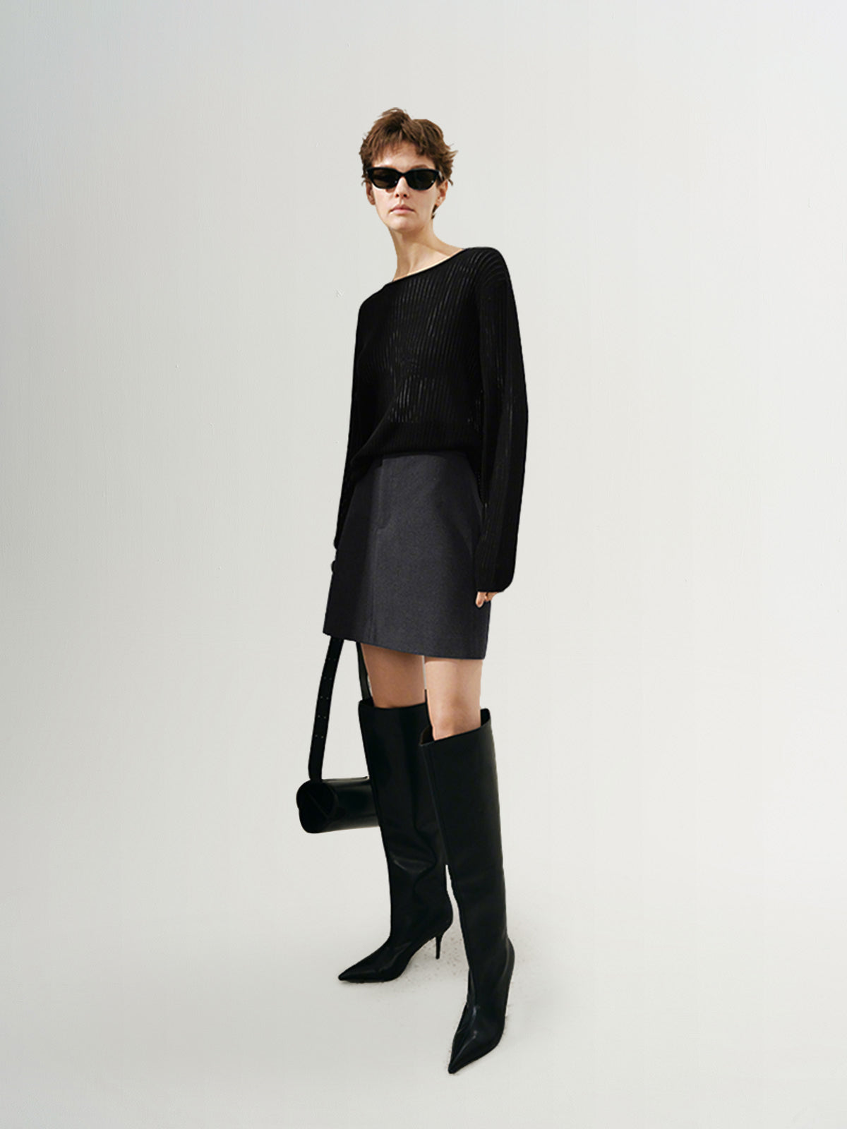 Model wearing a rib knit sweater with a relaxed silhouette, paired with a skirt and knee-high boots in a stylish pose.
