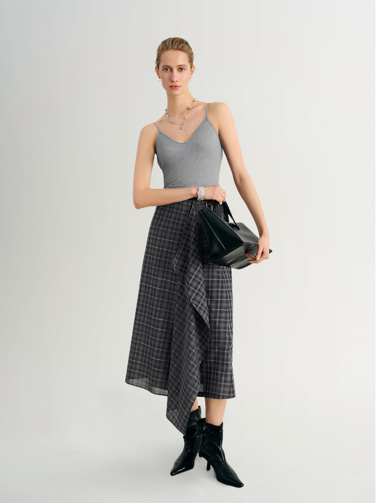 Woman wearing a gray top and plaid skirt holding a black handbag on a white background