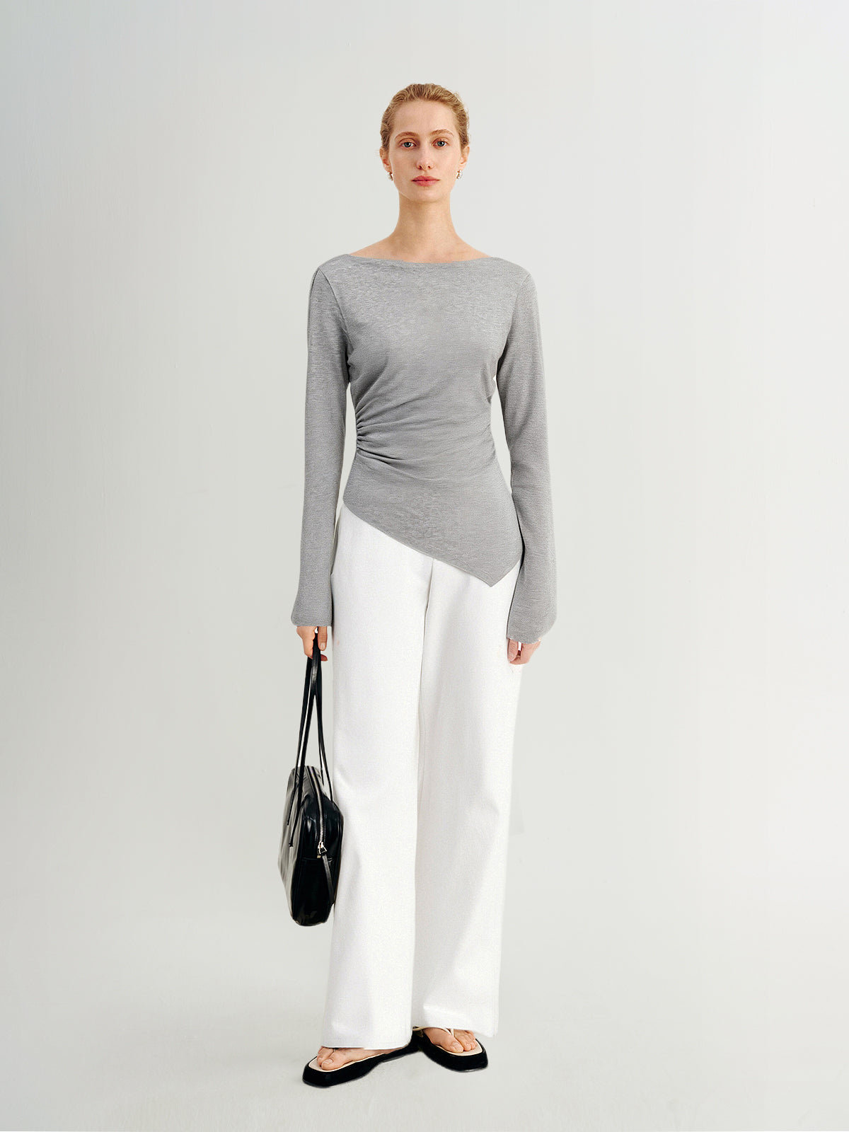 Woman wearing a gray long-sleeve top and white pants on a light gray background
