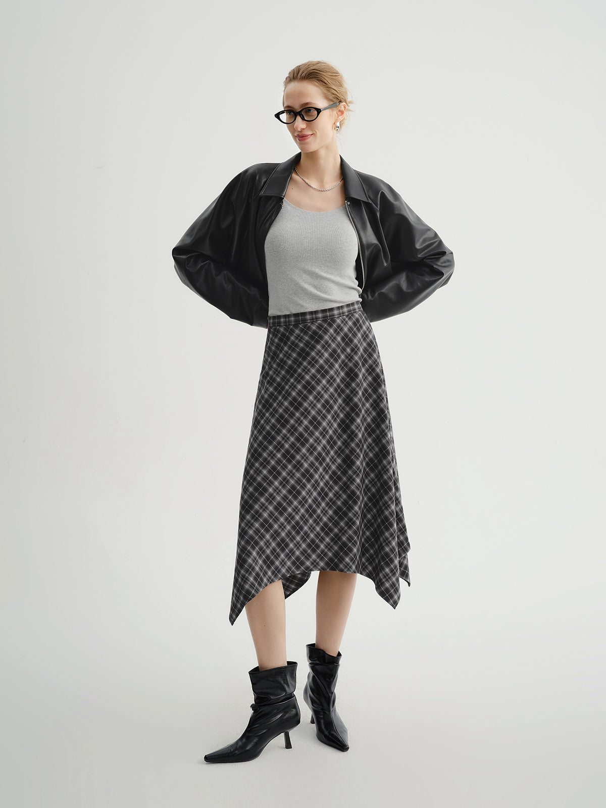 Model wearing a black jacket, gray top, plaid skirt, and black boots