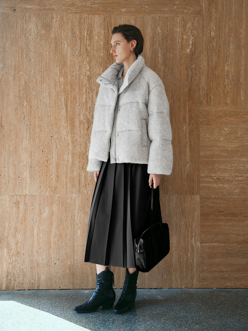 Person wearing a light gray puffer coat against a wooden wall