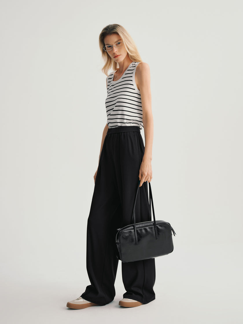 Woman wearing a striped top and black wide-leg pants holding a black handbag on a light gray background
