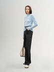 Woman wearing a light blue sweater and black pants against a plain background