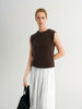 Woman wearing a brown sleeveless top and white pleated skirt on a plain background