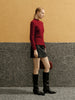 Woman wearing a red sweater and black skirt against a yellow and gray wall.