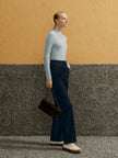 Woman in a light gray turtleneck and dark blue jeans standing against a yellow and gray wall.