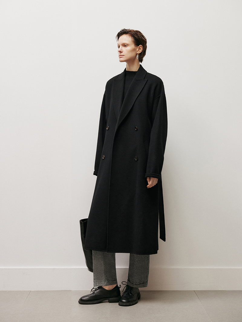 Women wearing a black coat standing against a white wall