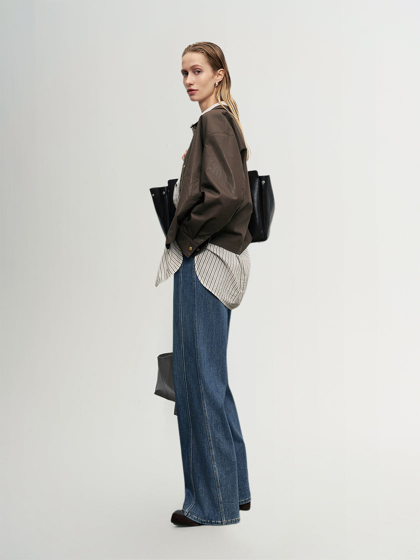 Woman wearing a brown jacket, striped shirt, and blue jeans against a white background