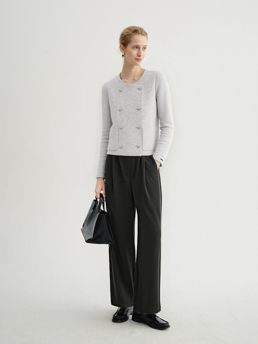 Woman wearing a gray cardigan, black pants, and holding a black handbag on a white background