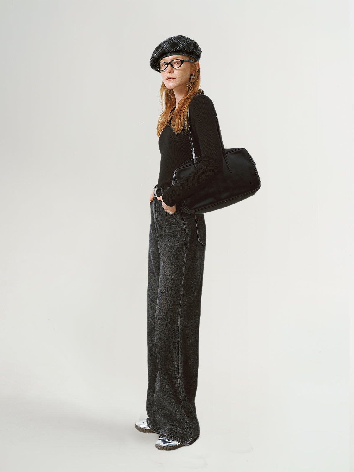 Person wearing a black outfit with a beret and holding a black bag on a white background