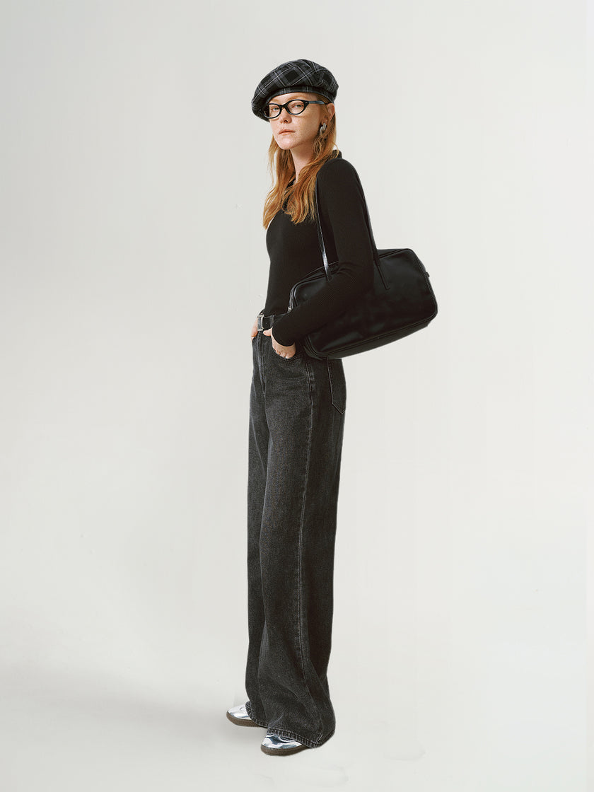 Person wearing a black outfit with a beret and holding a black bag on a white background