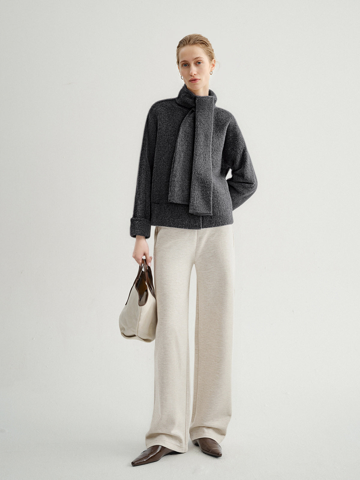 Woman wearing a dark gray jacket and light beige pants on a white background