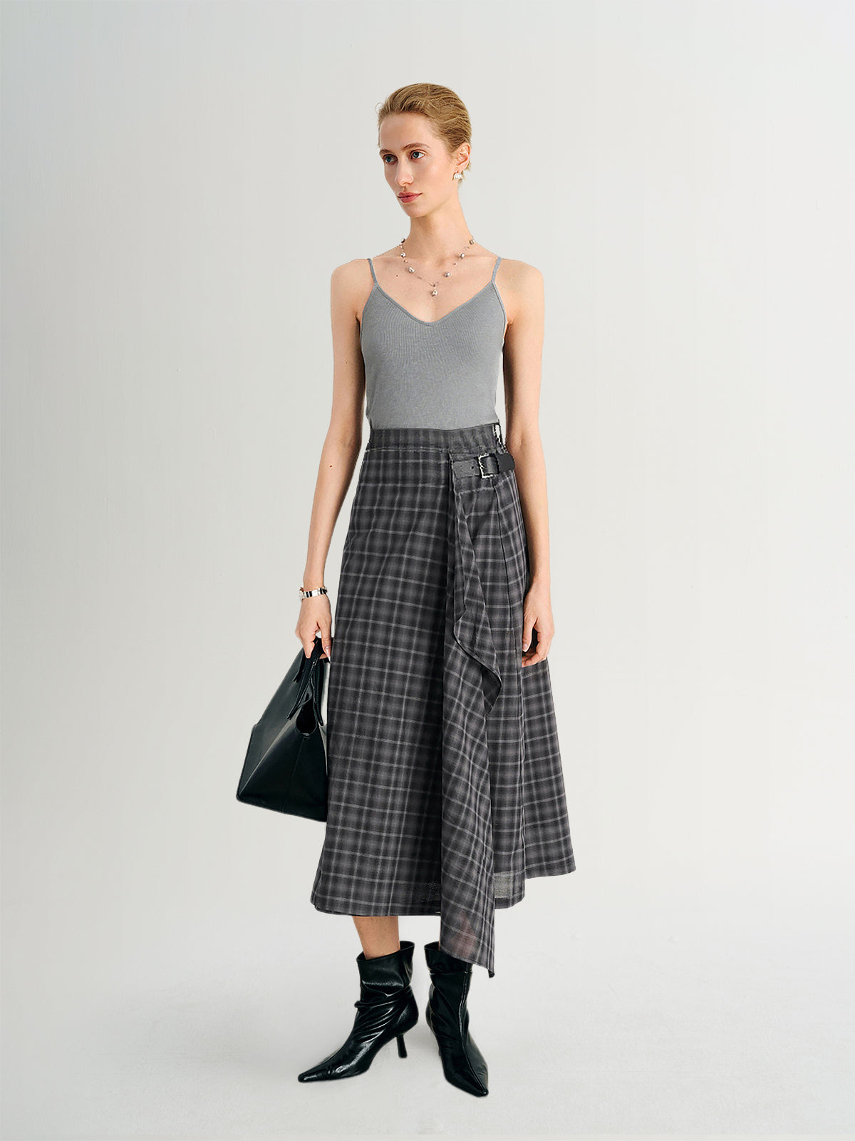 Woman wearing a gray tank top and plaid skirt with black boots on a white background