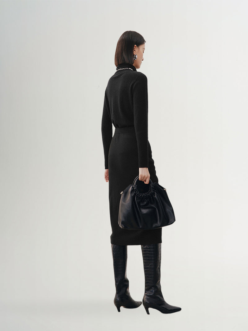 Woman wearing a black high neck layering cashmere sweater and holding a black handbag.