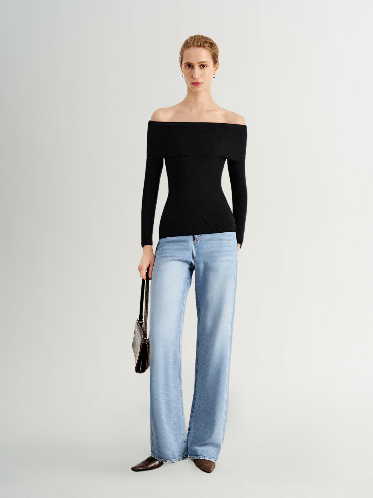 Woman wearing a black off-shoulder top and light blue jeans on a white background