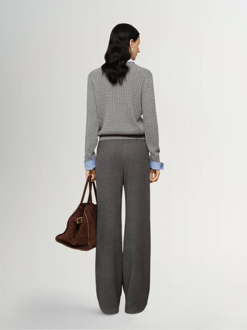 Woman wearing a gray checkered sweater and gray pants, holding a brown handbag on a white background