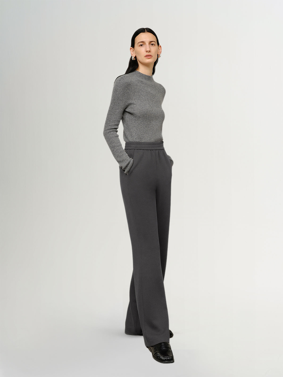 Person wearing a gray sweater and dark gray pants on a white background