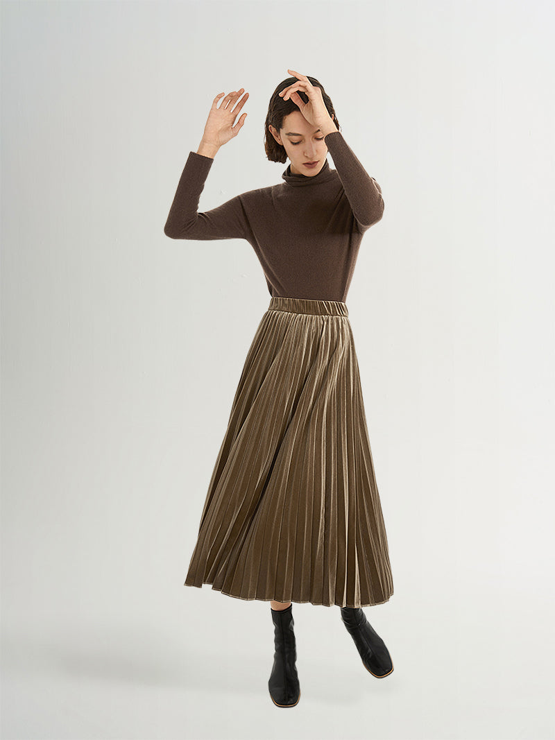 Model wearing a brown cashmere sweater and pleated midi skirt with high neck design, showcasing elegance and style.