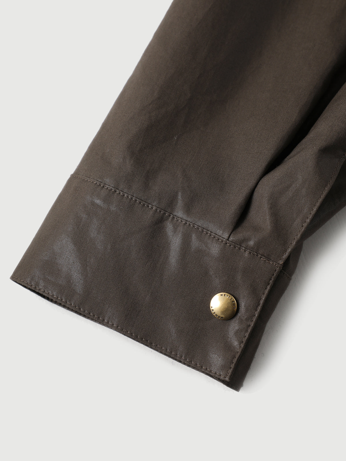 Close-up of a brown jacket sleeve with a gold button on a light gray background