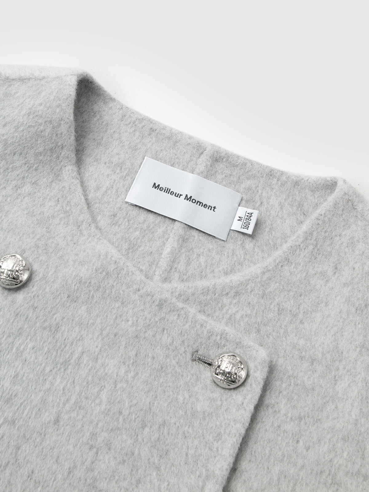 Gray garment with silver buttons and a visible brand label on a light gray background