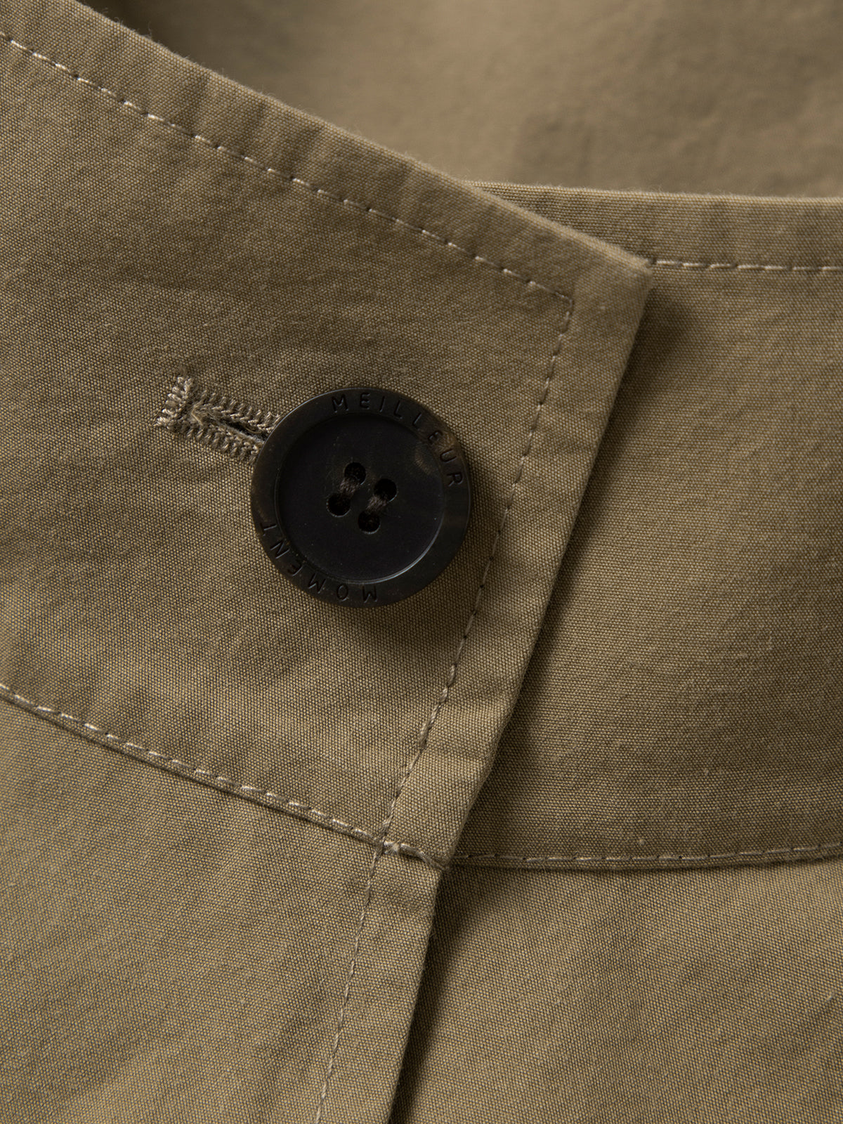 Close-up of a button on a beige fabric with a brand logo.