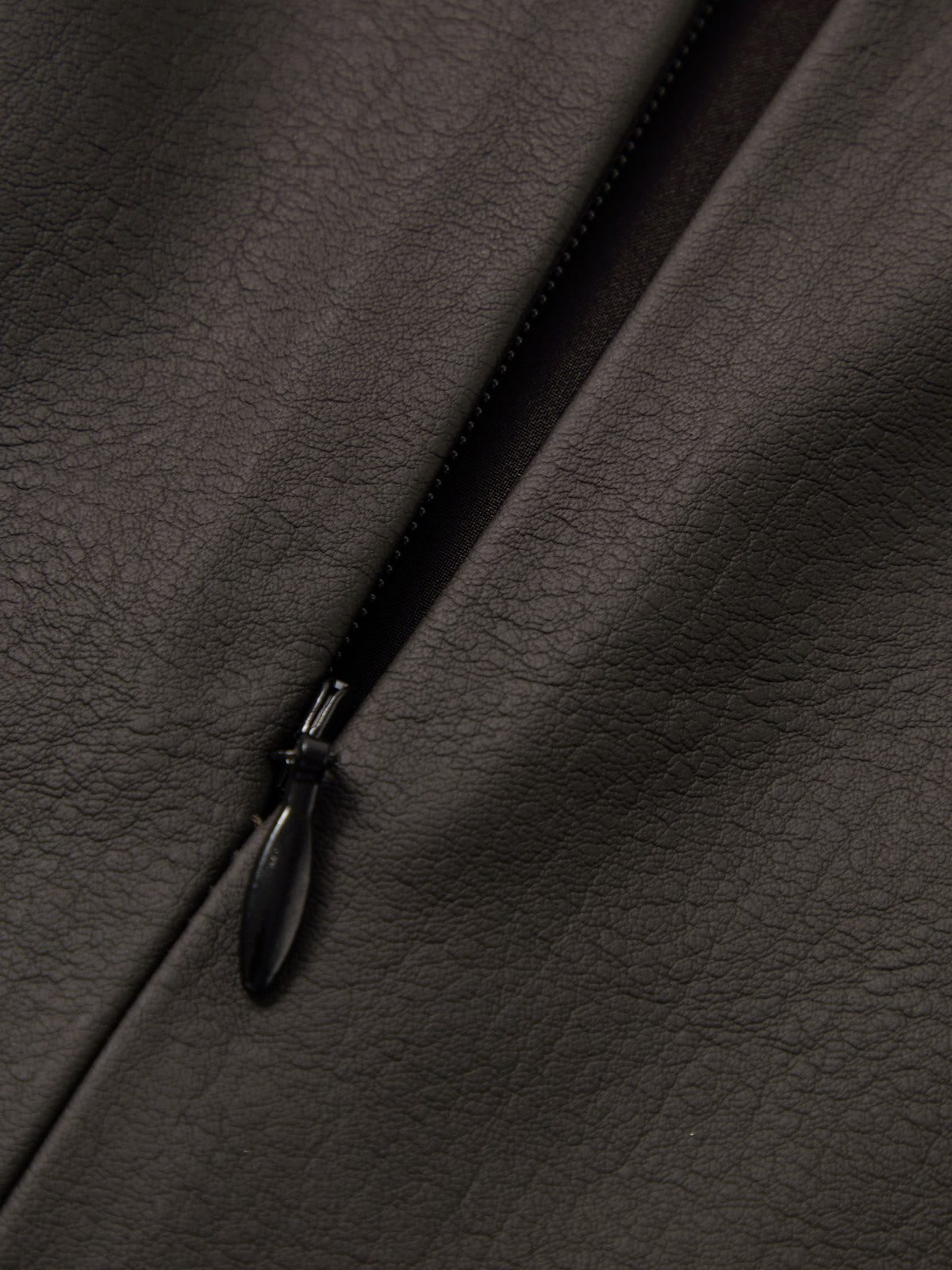 Close-up of a black zipper on dark brown leather fabric
