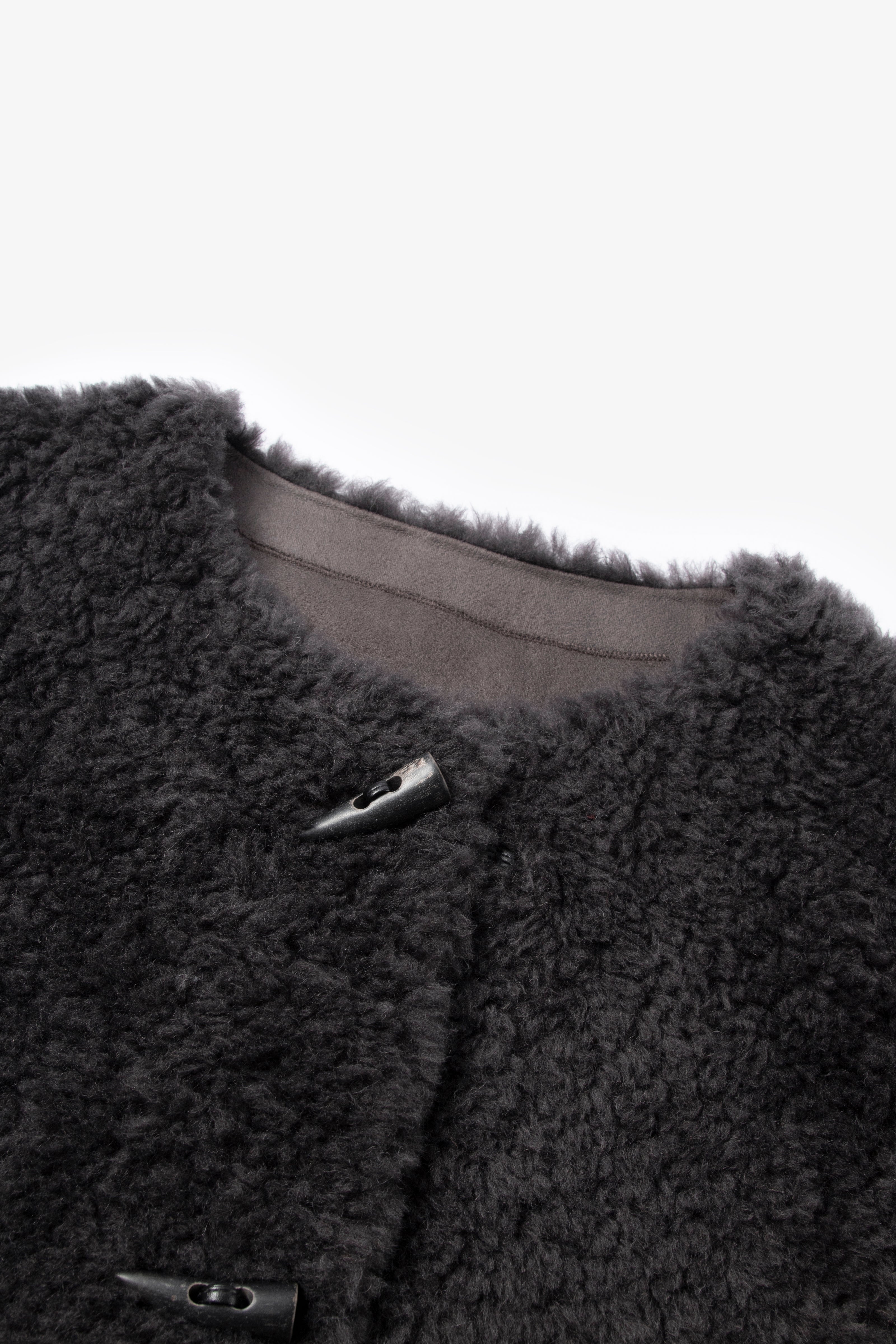 Close-up of a dark gray fleece jacket with buttons on a light gray background