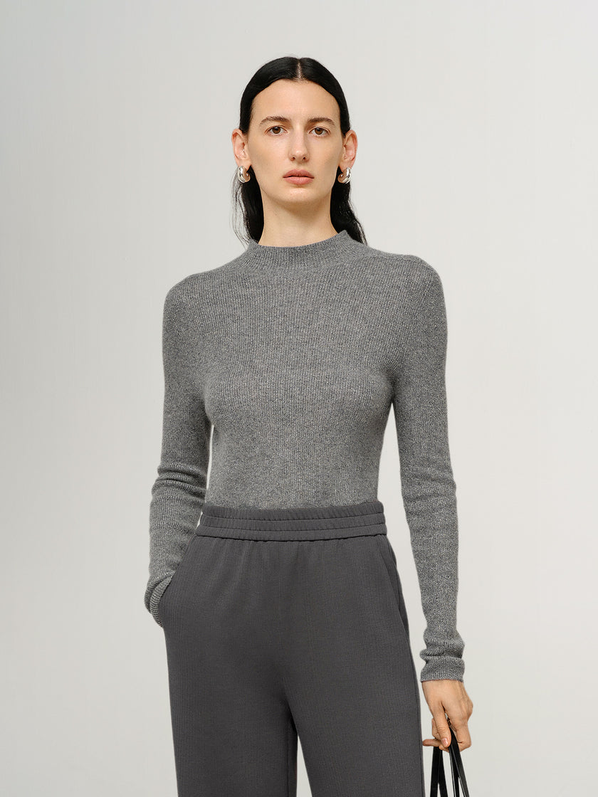 Woman wearing a gray long-sleeve top and pants against a light gray background