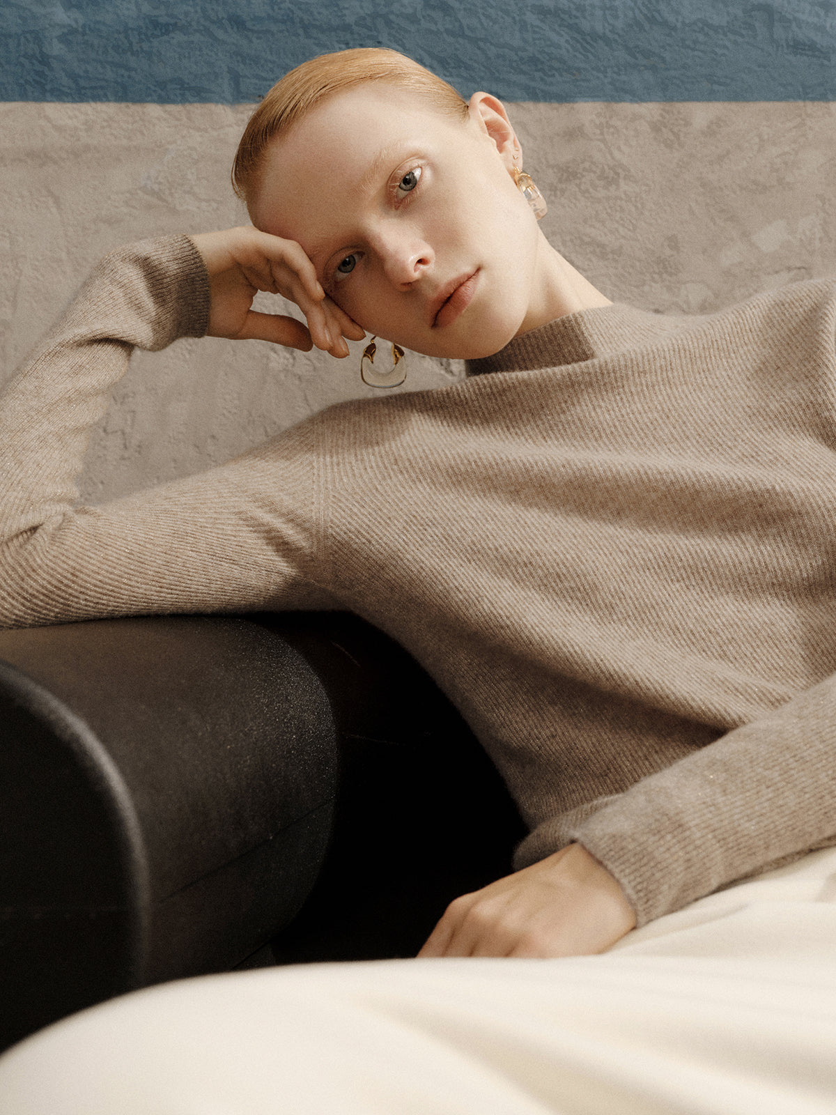 Person wearing a beige sweater sitting on a couch with a neutral background