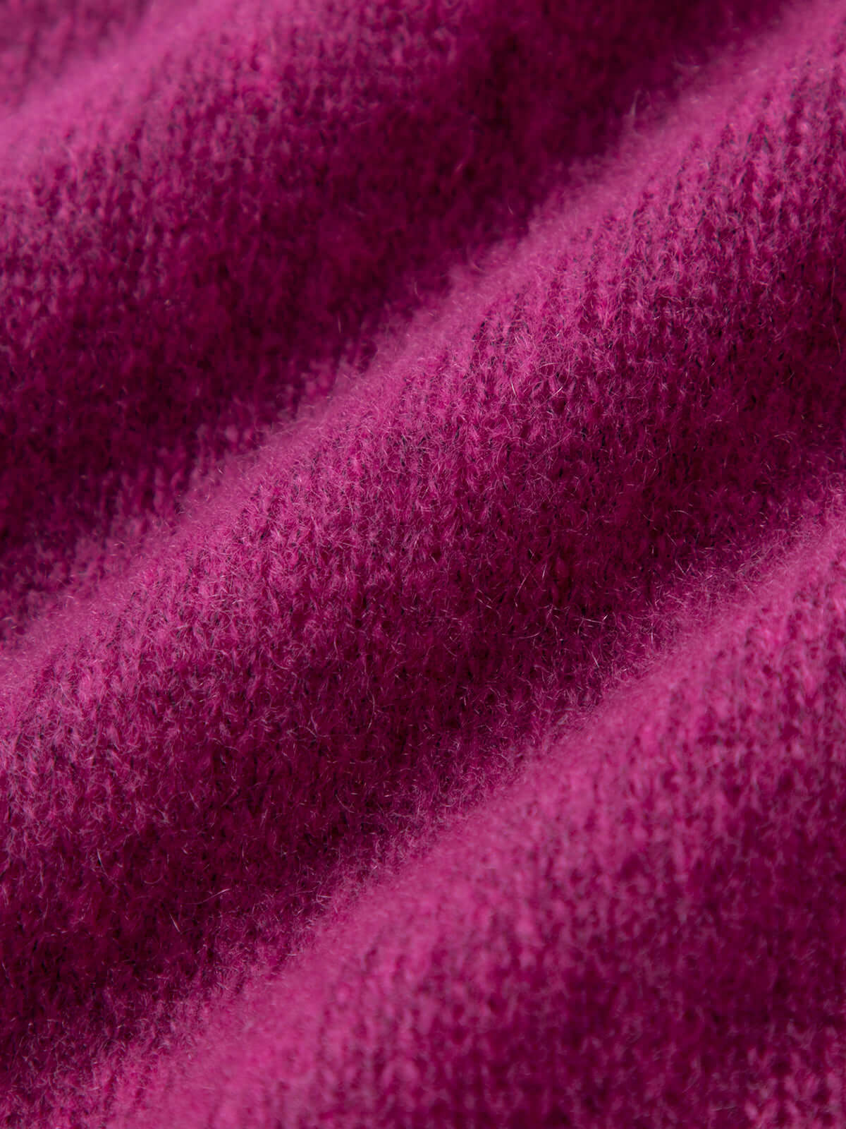 Close-up texture of a luxurious silk-cashmere cardigan fabric in rich fuchsia hue.