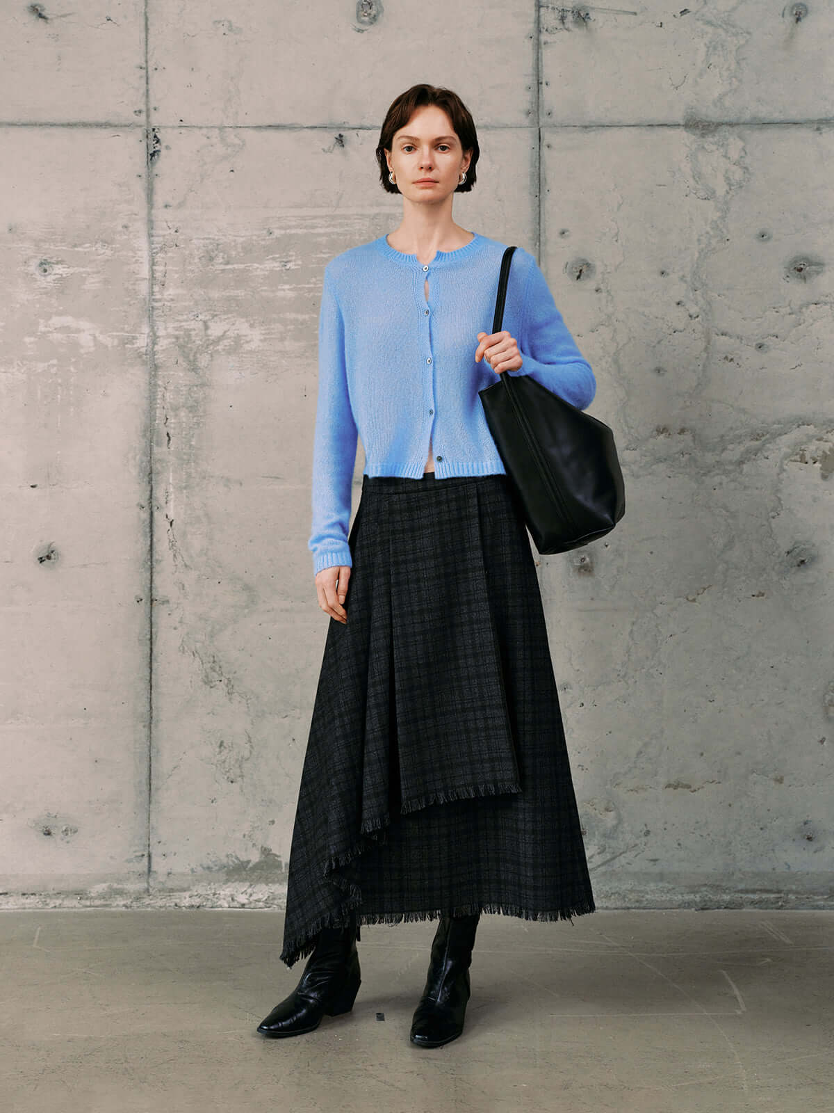 Model wearing a Silk-Cashmere Cardigan in soft blue, paired with a black plaid skirt and stylish accessories.