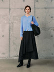 Model wearing a Silk-Cashmere Cardigan in soft blue, paired with a black plaid skirt and stylish accessories.