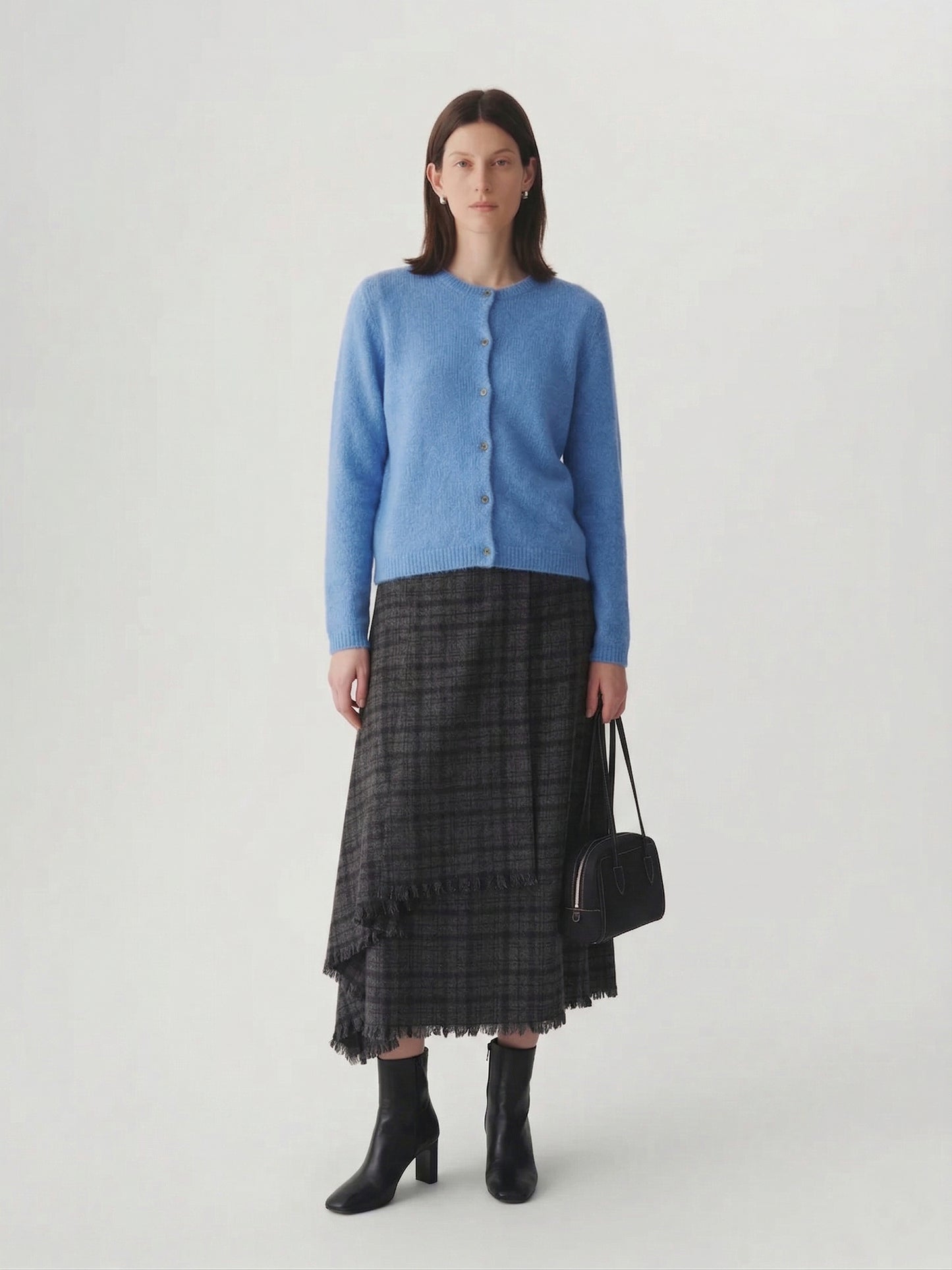 Silk-Cashmere Cardigan in soft blue hue worn with a plaid skirt, showcasing versatility for layered outfits.