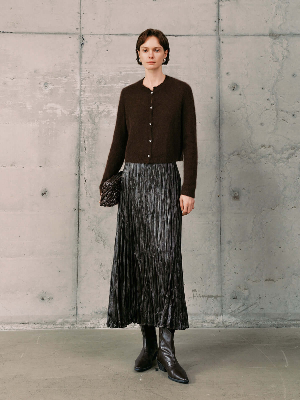 Silk-Cashmere Cardigan styled with a pleated skirt and knee-high boots against a concrete backdrop.