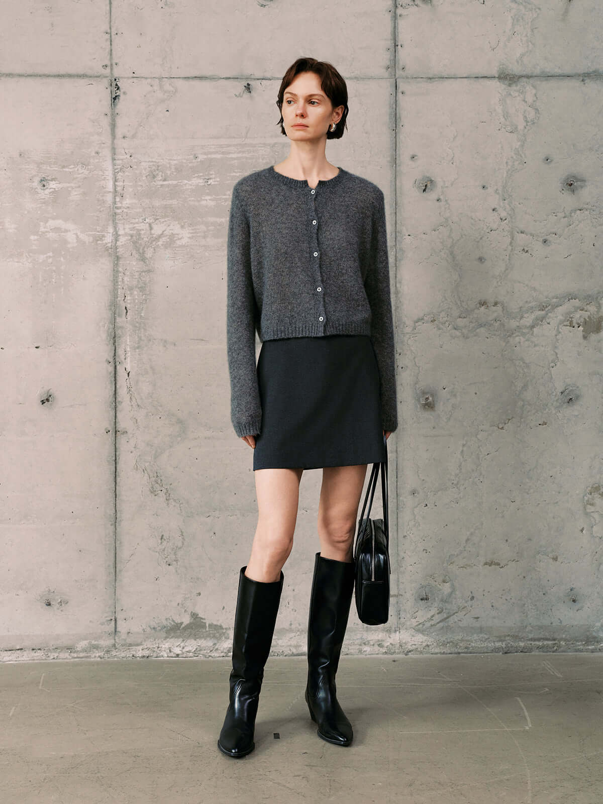 Silk-Cashmere Cardigan styled with a black skirt, boots, and a handbag against a textured concrete background.