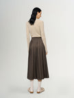 Woman wearing a beige sweater and brown pleated skirt on a white background