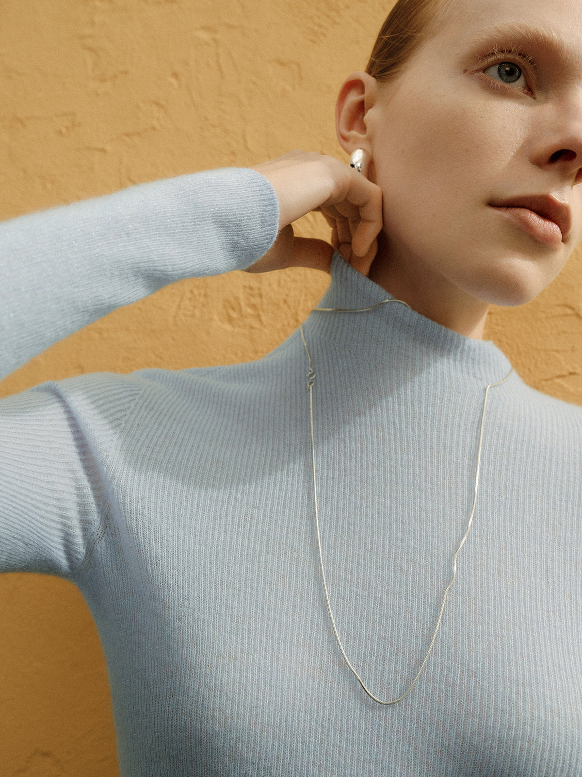 Woman wearing a light blue sweater and silver necklace against a beige background