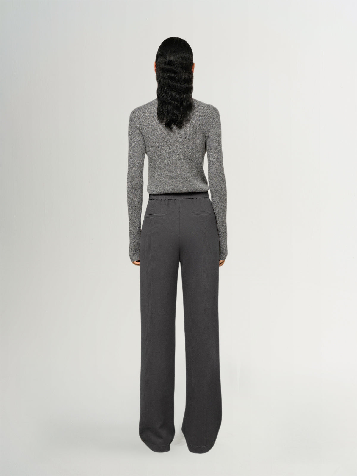 Person wearing a gray sweater and dark gray pants on a white background